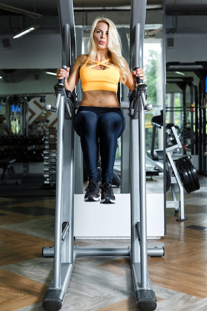 Athletic blonde woman using press machine in gym