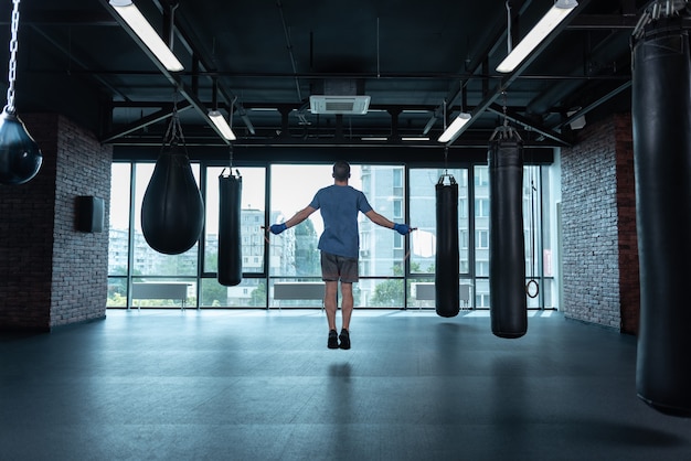 Athletic boxer. Athletic professional strong boxer wearing blue wrist wraps jumping rope while training hard