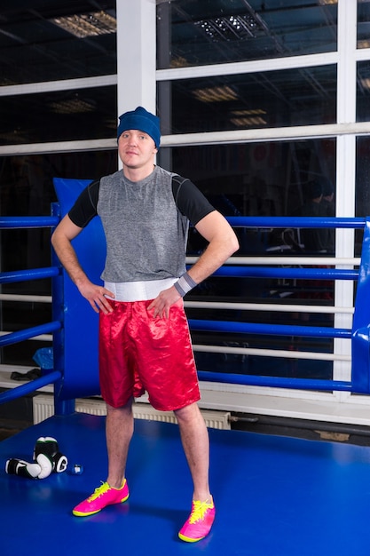 Athletic boxer standing in a regular boxing ring surrounded by ropes in a gym