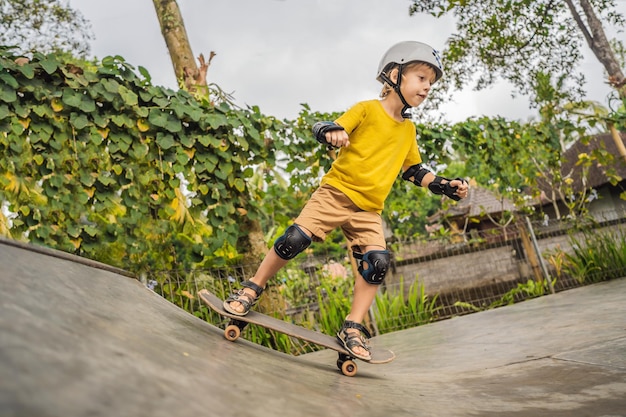 Athletic boy in helmet and knee pads learns to skateboard with in a skate park Children education sports