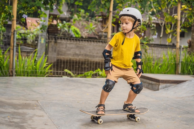 Athletic boy in helmet and knee pads learns to skateboard with in a skate park Children education sports