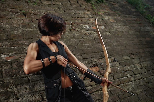 Photo athletic brunette shooting with bow and tacking focus.