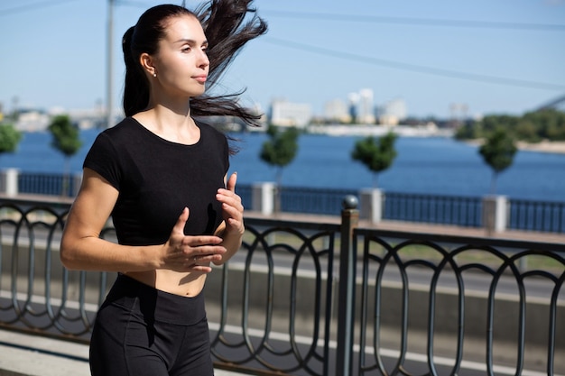 Athletic brunette woman running on the bridge near the river. Space for text