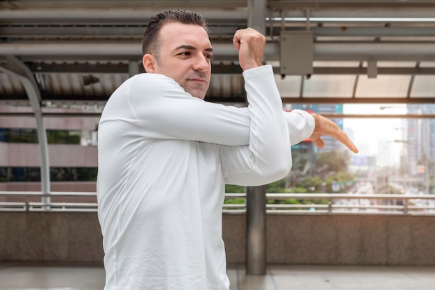 Athletic Caucasian man stretching body, doing exercises on street.