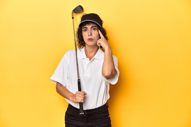 Photo athletic caucasian woman with curly hair golfing in studio pointing temple with finger thinking