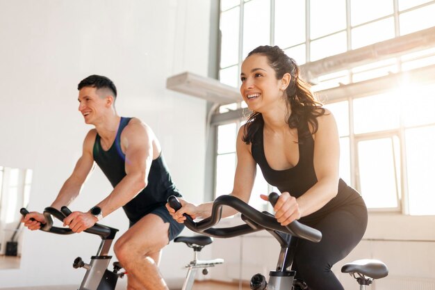 Photo athletic couple of cyclists train on static bicycle simulator man trainer and fitness woman