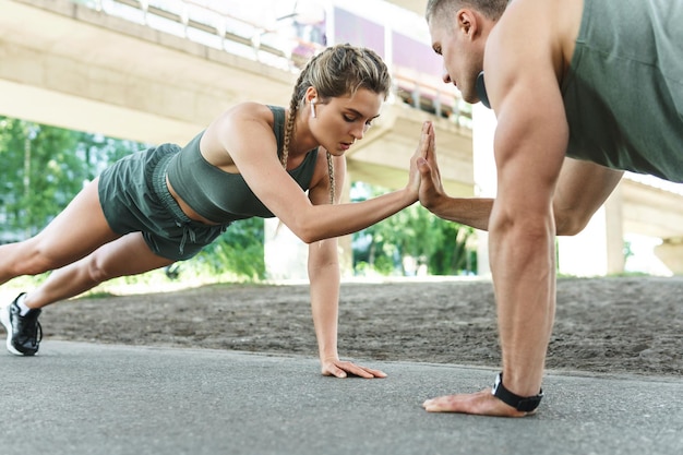 Athletic couple and fitness training outdoors. Man and woman doing push-ups exercise for chest and triceps muscles during street workout