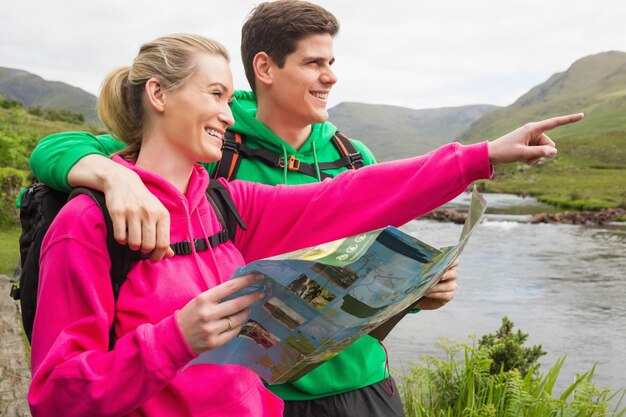 Photo athletic couple in hooded jumpers on a hike holding map