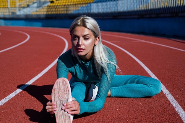 Athletic female coach in fitness costume stretch on running track flexibility