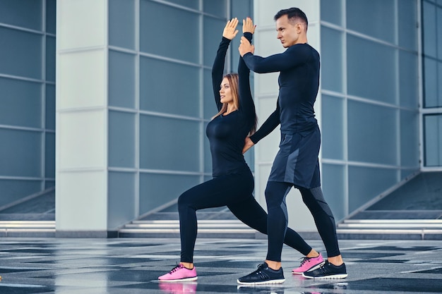 The athletic fitness couple is stretching over modern building background. Full body image.