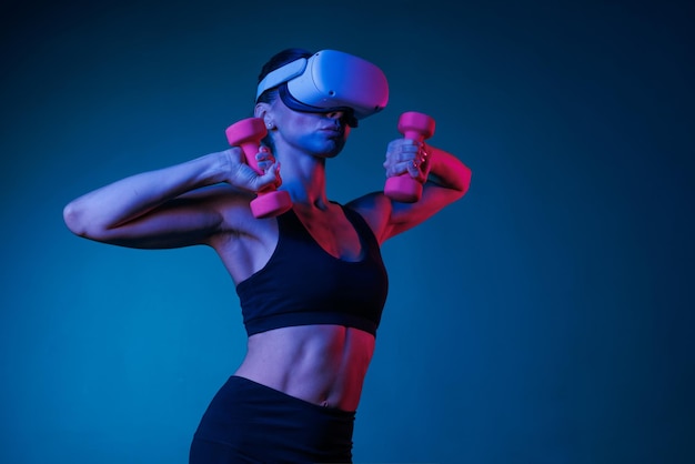 athletic girl doing online training in VR glasses in black clothes with dumbbells on a dark background online sports training