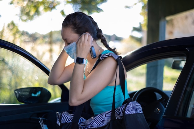 車から降りて、トレーニングに行くために彼女のマスクを身に着けている運動の女の子。