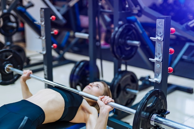 Athletic girl raises barbell lying on the bench on the simulator in the gym.