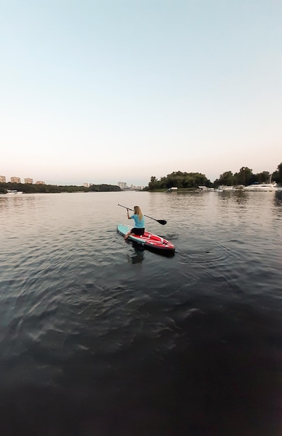 Спортивная девушка плавает на доске для плавания SUP на коленях и гребет веслом