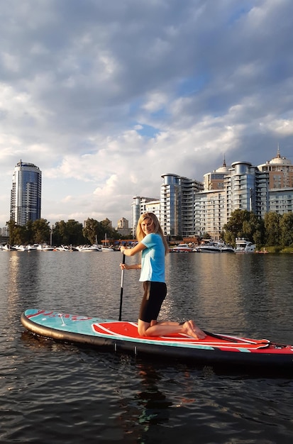 Athletic girl swims on a SUP board while kneeling and smiling