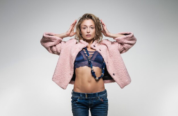 Photo athletic girl with blond hair in a fur pink jacket on a white background