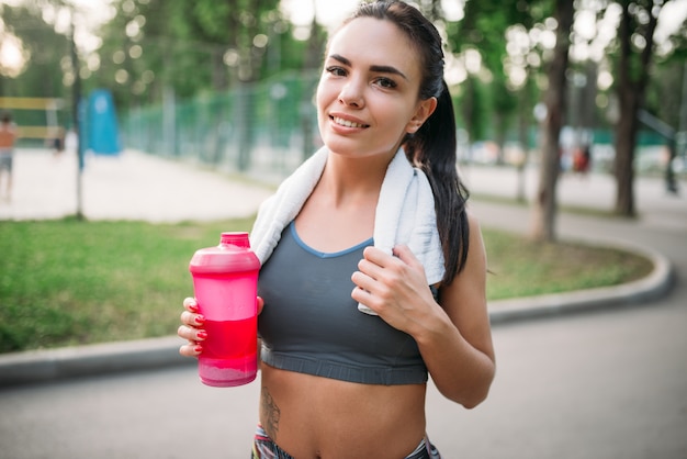 夏の公園でスポーツボトルを持つ運動少女。朝の運動の女性