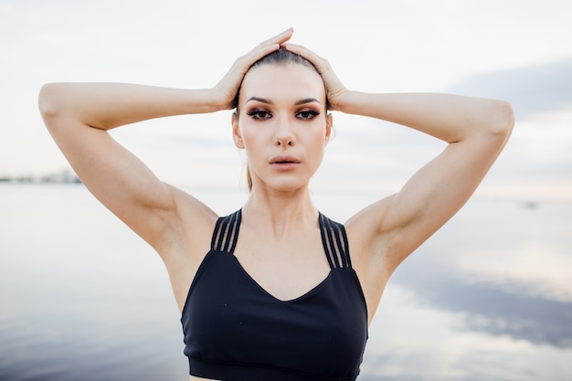 Athletic girl with tank top doing a stretch on the beach