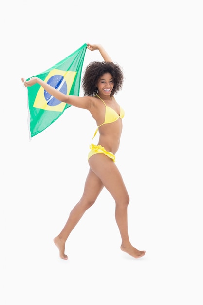 Athletic girl in yellow bikini holding brazil flag