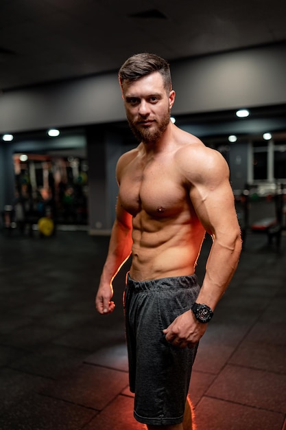 Athletic guy is looking to the camera. Big muscles, strong abs. Handsome sportive model on the gym background.