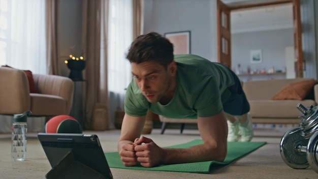 タブレットでオンラインレッスンを見ているヨガマットで板を練習しているアスリートの男