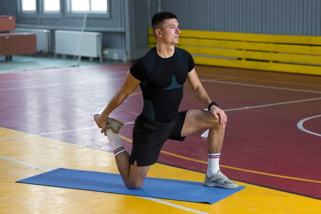 Спортивный парень в спортивной одежде и фитнес-трекере делает упражнения в тренажерном зале.