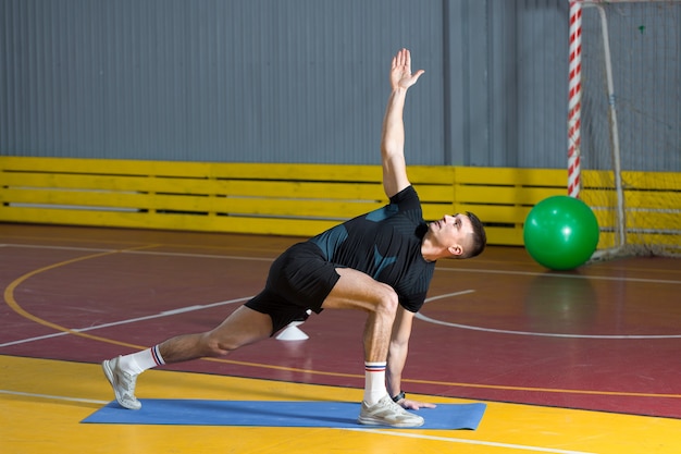 Спортивный парень в спортивной одежде и фитнес-трекере делает упражнения в тренажерном зале.