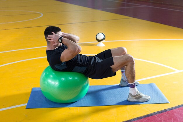 Спортивный парень в спортивной одежде и фитнес-трекере делает упражнения в тренажерном зале.