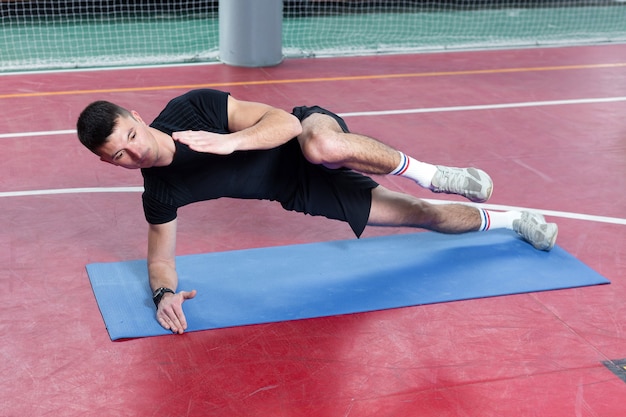 Athletic guy in sportswear and fitness tracker doing exercises in gym.