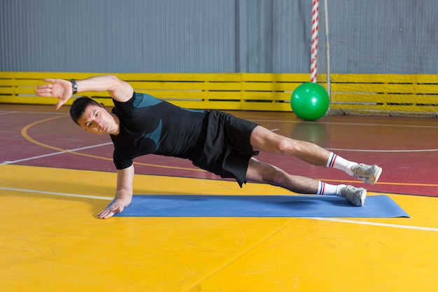 Спортивный парень в спортивной одежде и фитнес-трекере делает упражнения в тренажерном зале.