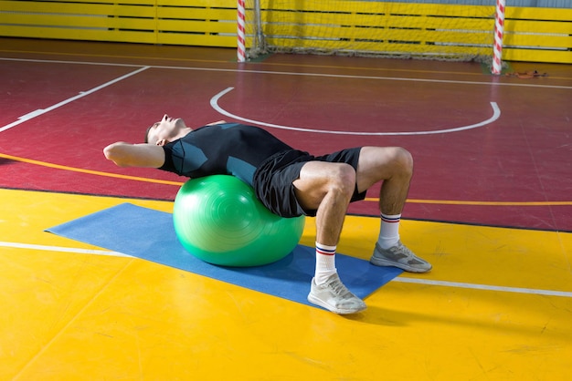Спортивный парень в спортивной одежде и фитнес-трекере делает упражнения в тренажерном зале.