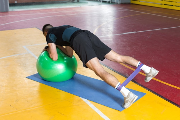 Спортивный парень в спортивной одежде и фитнес-трекере делает упражнения в тренажерном зале.