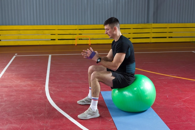 Спортивный парень в спортивной одежде и фитнес-трекере делает упражнения в тренажерном зале.