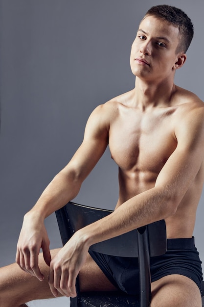 Athletic man in black panties pumped up body sits on a chair