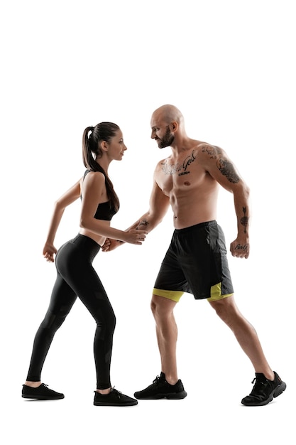 Athletic man in black shorts and sneakers with brunette woman in leggings and top posing isolated on