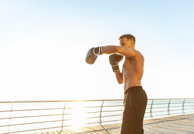 Атлетический мужчина в боксерских перчатках боксирует рано утром на пляже