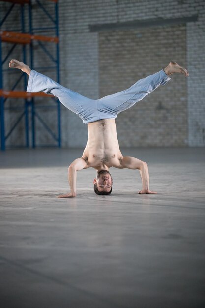 An athletic man on capoeira training standing on the hands with legs apart