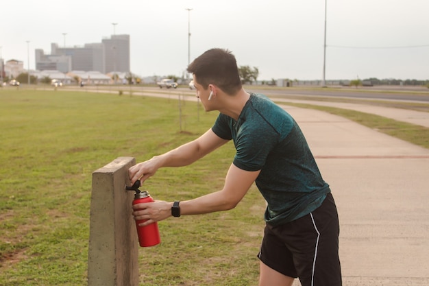 Спортивный мужчина несет воду из общественного питьевого фонтана, слушая музыку в наушниках.