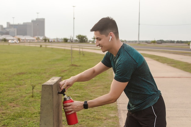 Спортивный мужчина несет воду из общественного питьевого фонтана.