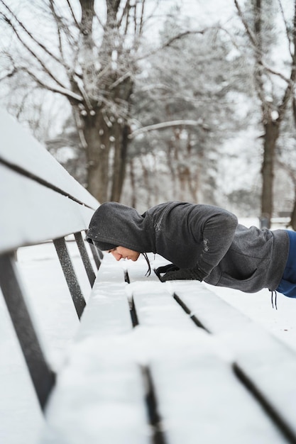 雪に覆われた都市公園で彼の体操の冬のトレーニング中に腕立て伏せをしている運動選手