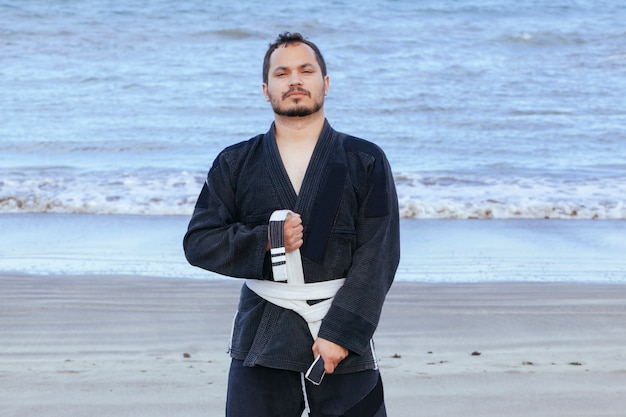 Спортивный человек, одетый в кимоно тхэквондо, изолированное на пляже