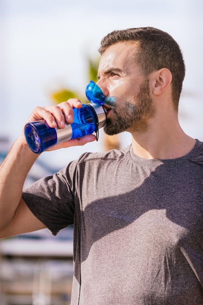 athletic man drinking water from red bottle outdoors in city park vertical