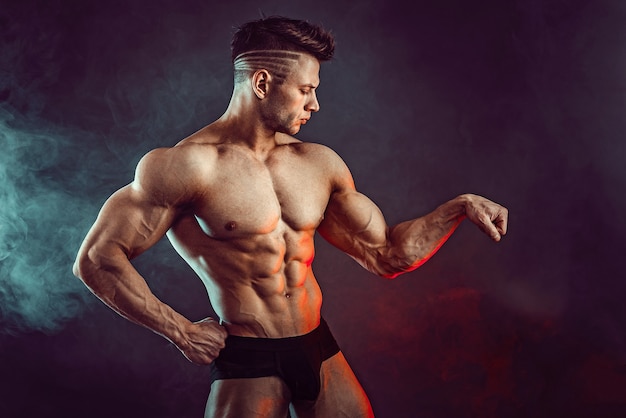 Athletic man flexing muscles  with smoke. Strong bodybuilder with perfect abs.