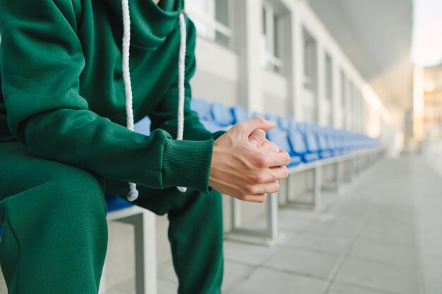 Athletic man in a green tracksuit sitting in the stands and resting after training