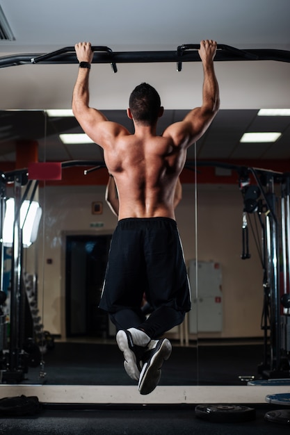 Athletic man making pull-up exercises on a crossbar in the gym