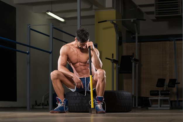 Athletic Man Resting  Workout At Gym With Hammer And Tractor Tire