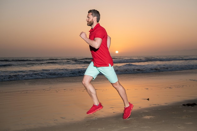 Athletic man runner running on sunset summer beach athlete