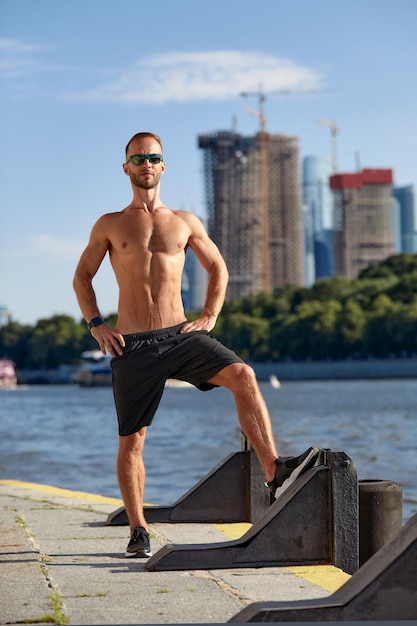 Athletic man running and doing functional workout outdoors Sportive adult male with sportswear training in a city on the river bank