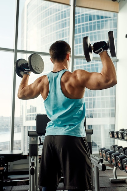 Athletic man shakes his biceps with dumbbell in his hands Healthy lifestyle concept