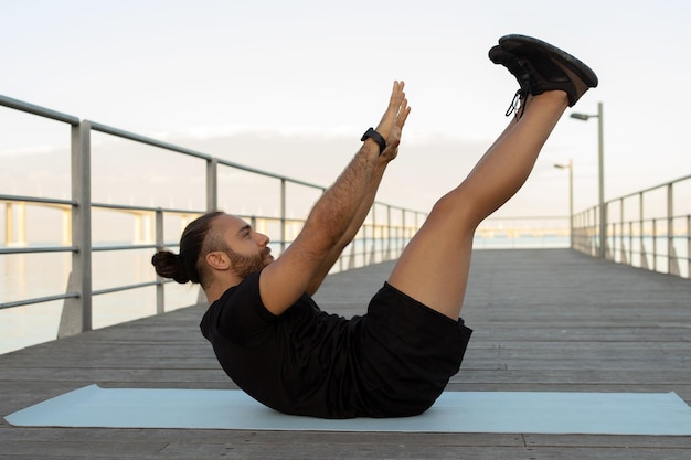 Foto uomo atletico che si allunga e raggiunge le dita delle gambe sdraiato sul tappetino all'aperto